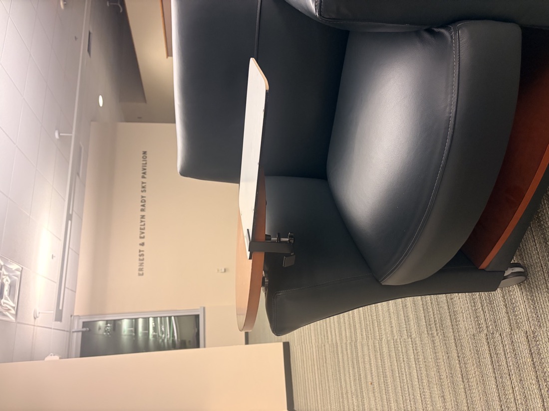 Side view of the ClipDesk prototype clamped to a lecture seat tablet arm with a bag hook below